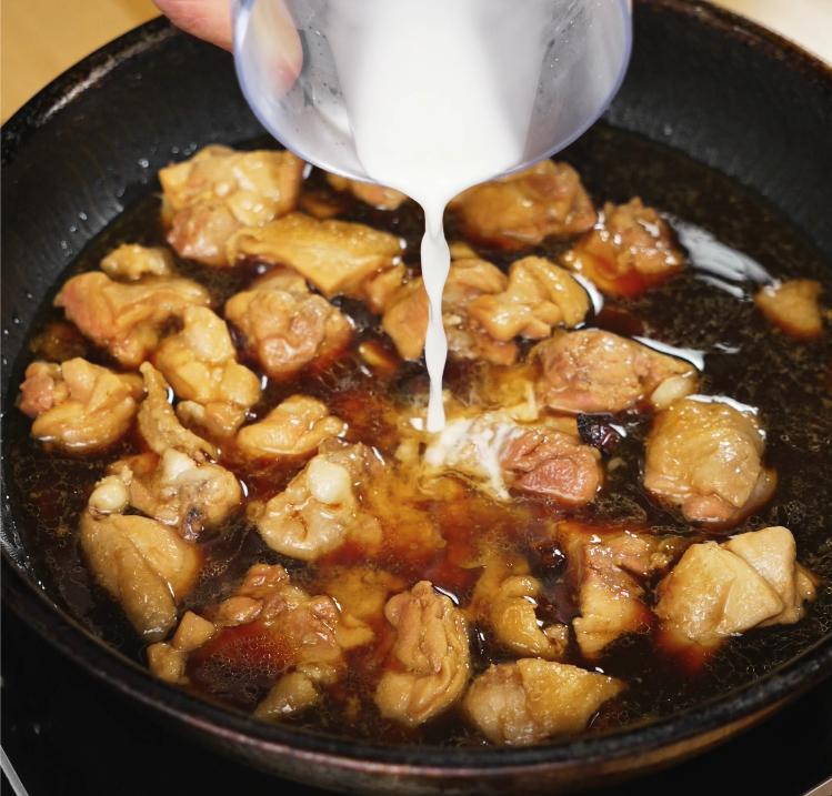 A cornstarch slurry is being poured into the simmering ginger soy chicken mixture, helping thicken the sauce to a glossy finish.