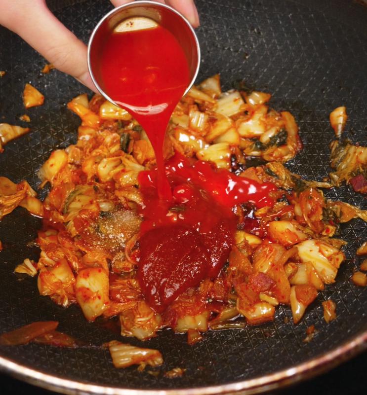 Gochujang paste and kimchi juice being poured into the sautéed kimchi and bacon mixture to form the sauce.