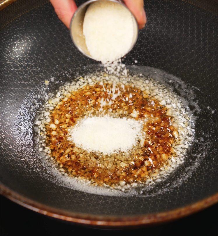 Parmesan cheese being sprinkled into a rich mixture of garlic and butter in a skillet, enhancing the umami of the garlic butter noodles.