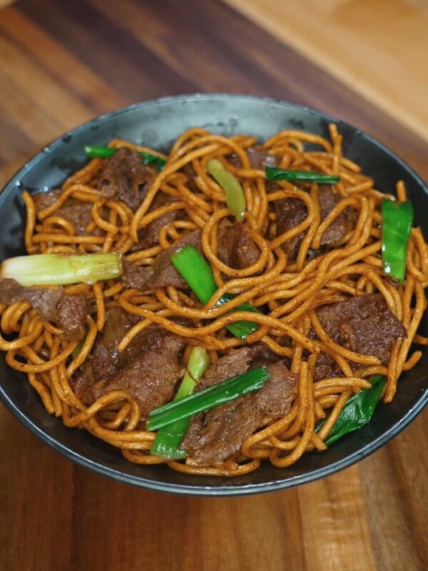 A finished bowl of beef lo mein featuring perfectly coated noodles, tender slices of beef, and vibrant green onions. This final presentation showcases the glossy sauce and balanced stir-fry technique.