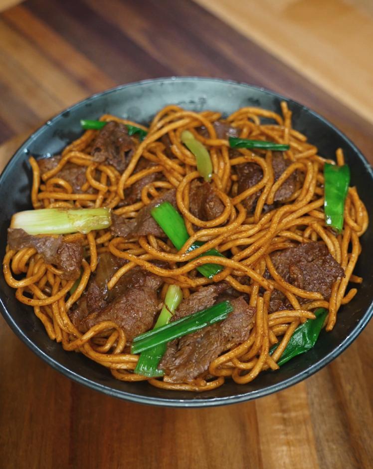 A finished bowl of beef lo mein featuring perfectly coated noodles, tender slices of beef, and vibrant green onions. This final presentation showcases the glossy sauce and balanced stir-fry technique.