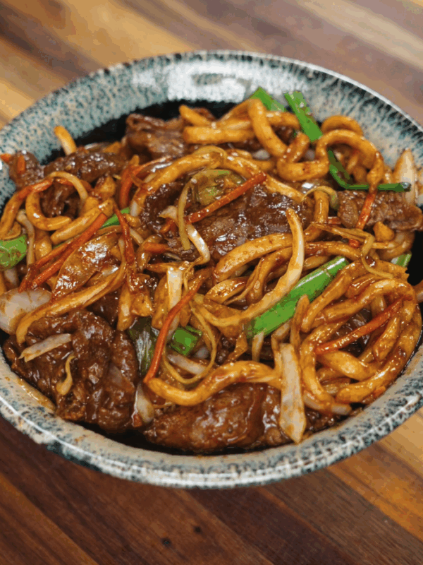A serving bowl of finished beef yaki udon packed with stir-fried beef, thick udon noodles, cabbage, and carrots in a glossy savory sauce.