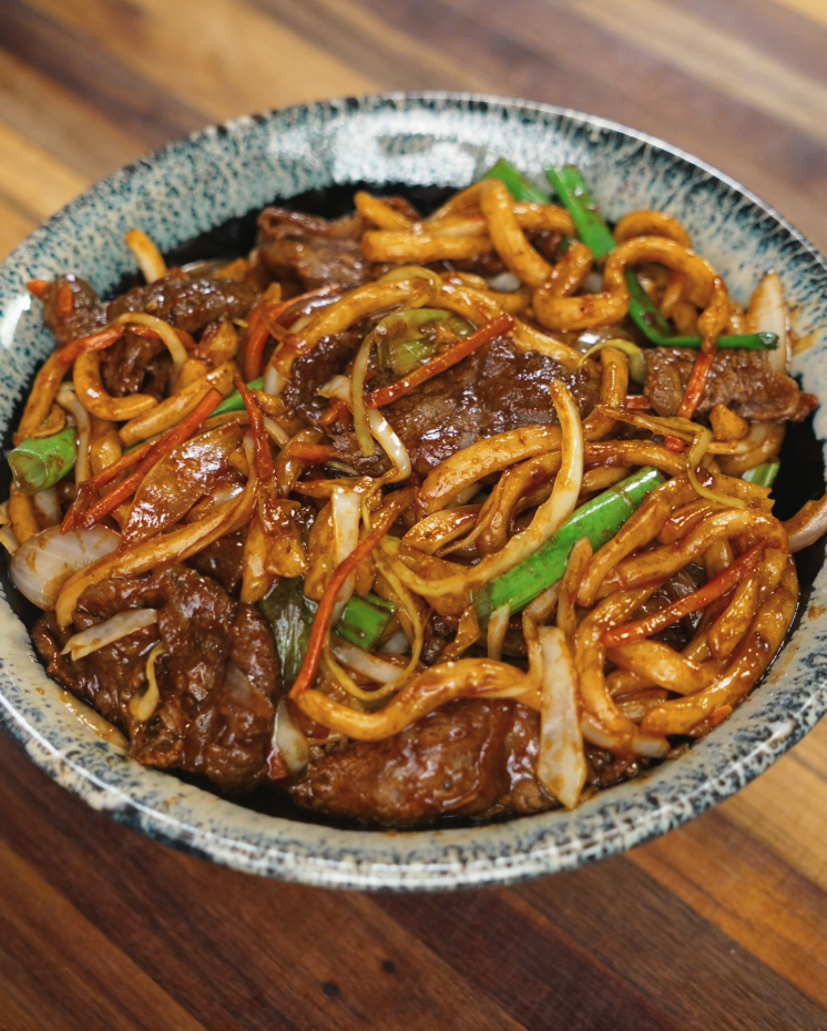 A serving bowl of finished beef yaki udon packed with stir-fried beef, thick udon noodles, cabbage, and carrots in a glossy savory sauce.