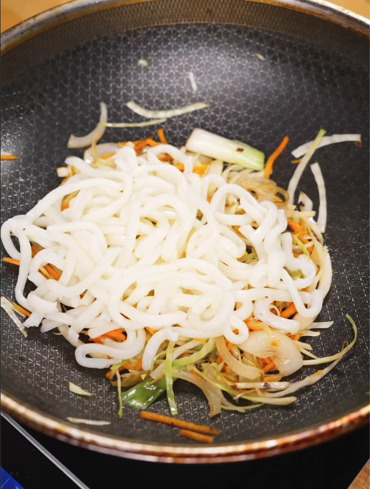 Fresh udon noodles added to a skillet of stir-fried shredded cabbage, carrots, and scallions before tossing them together for beef yaki udon.