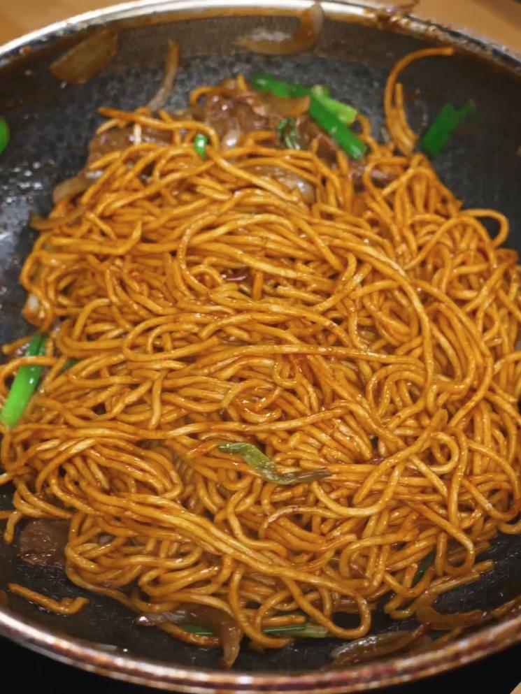Beef Lo Mein noodles being tossed in the marinated beef, sauce, onions, and green onions after being tossed very well until all ingredients are tossed well like a Chinese takeout dish.