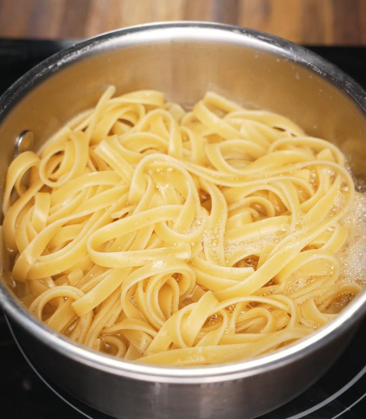 A stainless steel pot filled with fettuccine noodles boiling in hot water, showing the pasta just before being drained for the Gochujang Alfredo recipe.