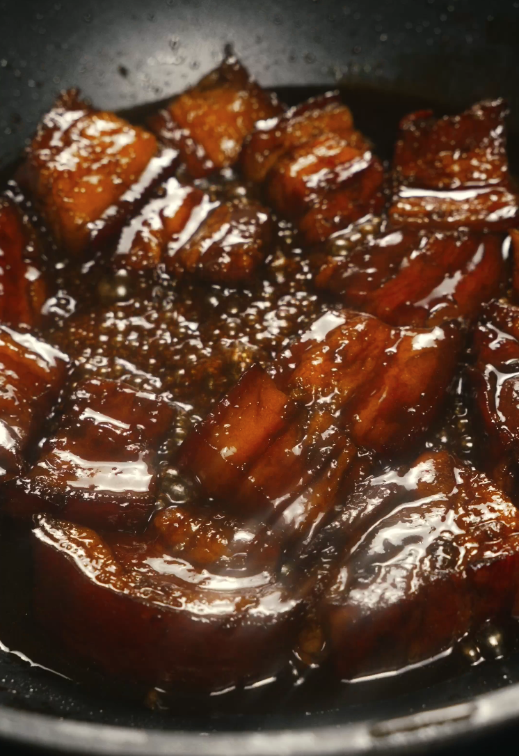 Chunks of pork belly simmering in a thick, glossy braising sauce, soaking in deep soy-based flavors.