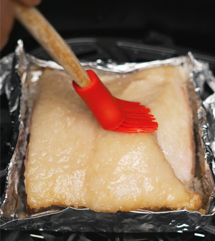 A red silicone brush applying a thin coat of oil onto the pork belly skin to help crisp it up during the final air fry stage.