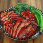 Char siu pork served sliced over steamed white rice with blanched Chinese greens, showcasing the glossy caramelized exterior and juicy interior of the pork.