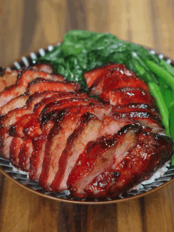 Char siu pork served sliced over steamed white rice with blanched Chinese greens, showcasing the glossy caramelized exterior and juicy interior of the pork.