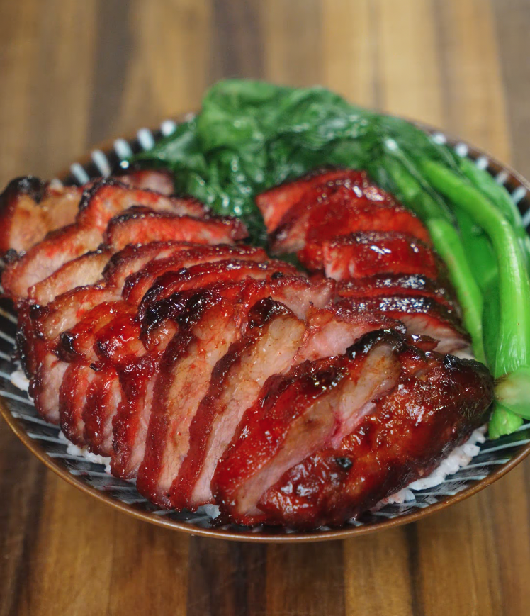 Char siu pork served sliced over steamed white rice with blanched Chinese greens, showcasing the glossy caramelized exterior and juicy interior of the pork.