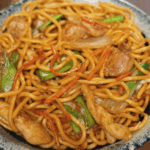 Close-up of Chicken Lo Mein served in a bowl, with glistening noodles, tender chicken, julienned carrots, and green onions tossed in savory sauce. A classic takeout-style dish made easily at home.