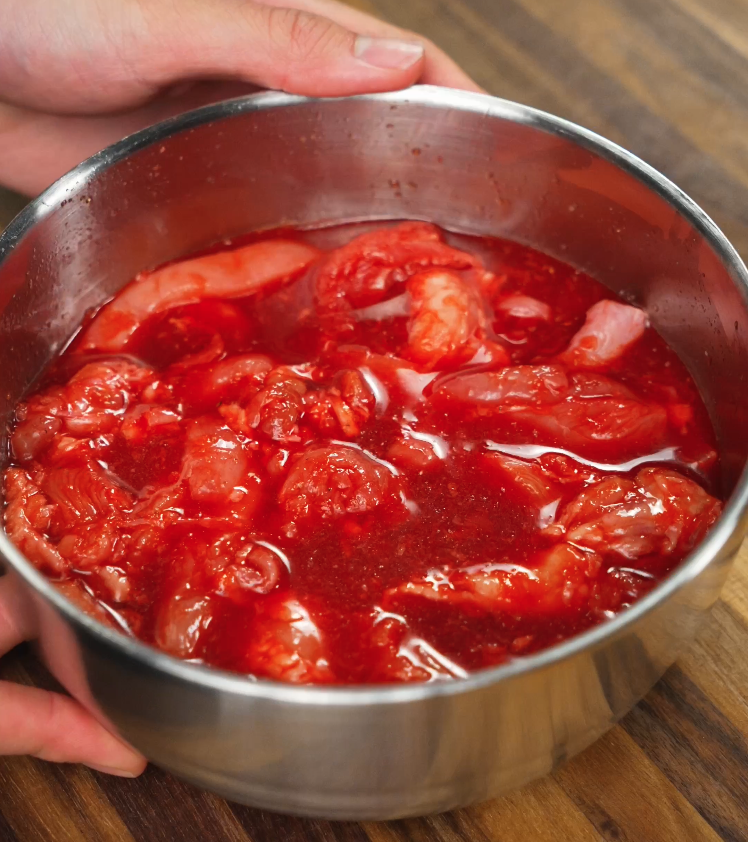 Raw chicken thighs fully coated in a vivid red marinade made with annatto powder, sugar, garlic, and pineapple juice. This step is crucial for flavor absorption and achieving the iconic red tocino color.