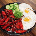 The finished Chicken Tocino bowl served with sunny-side-up eggs, sliced cucumbers, and scallions over white rice. The sweet and savory glazed chicken is caramelized perfectly, offering a classic Filipino breakfast presentation.
