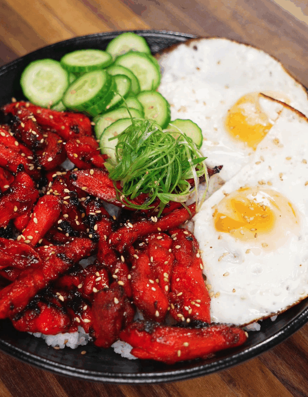 The finished Chicken Tocino bowl served with sunny-side-up eggs, sliced cucumbers, and scallions over white rice. The sweet and savory glazed chicken is caramelized perfectly, offering a classic Filipino breakfast presentation.