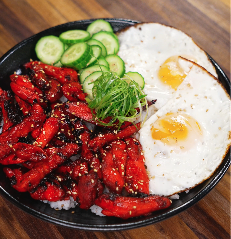 The finished Chicken Tocino bowl served with sunny-side-up eggs, sliced cucumbers, and scallions over white rice. The sweet and savory glazed chicken is caramelized perfectly, offering a classic Filipino breakfast presentation.