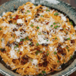 Final plated bowl of creamy chili oil caramelized onion pasta topped with grated parmesan, chili crisp, and chopped scallions.