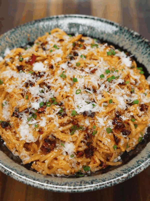 Final plated bowl of creamy chili oil caramelized onion pasta topped with grated parmesan, chili crisp, and chopped scallions.