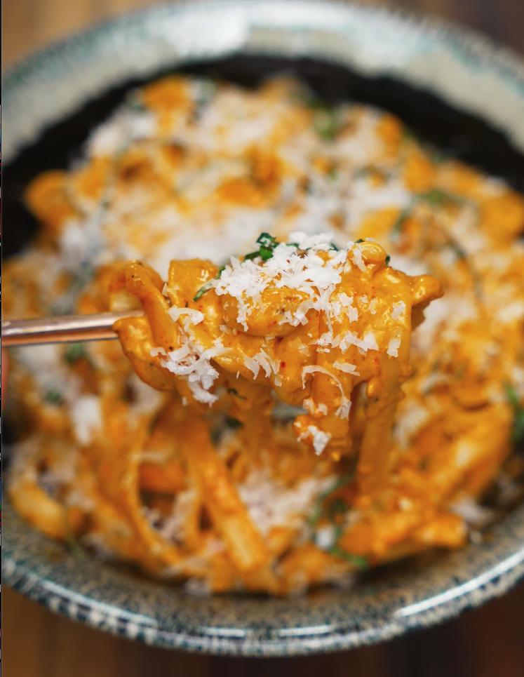 A mouthwatering bite of Gochujang Alfredo pasta being lifted from the bowl with chopsticks, showcasing the rich sauce and melted parmesan topping.
