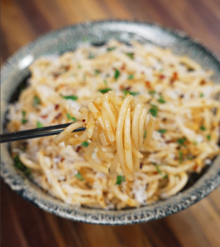 Chopsticks lifting a glossy bite of garlic butter noodles from the bowl, showcasing the perfect blend of butter, garlic, and chili flakes.