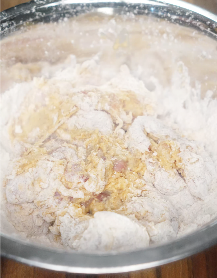 Chicken pieces being dredged in a flour and batter mixture, preparing them for deep frying.