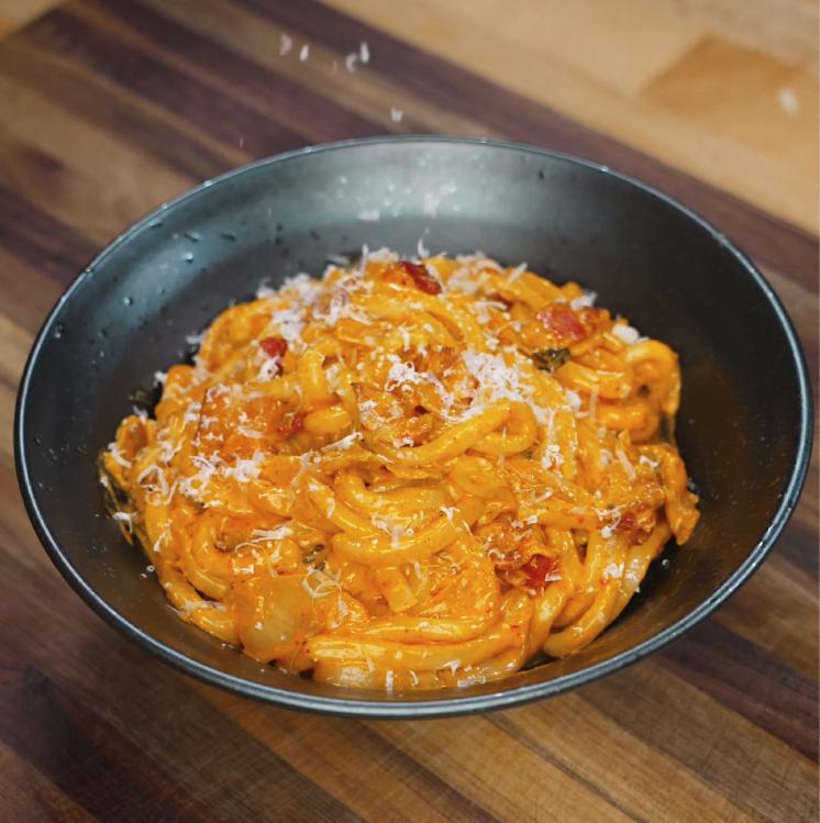 Creamy kimchi noodles plated in a bowl and sprinkled with shredded cheese just before serving.