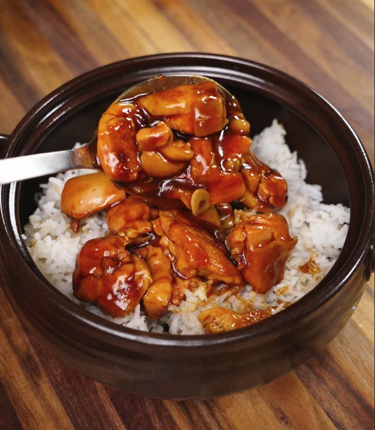 A spoonful of glossy, thick ginger braised chicken is being drizzled over a fresh bowl of steamed white rice, showcasing the final serving step.