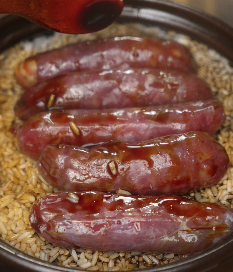 Soy sauce mixture being drizzled over the Chinese sausage on partially cooked rice, adding rich umami flavor to the claypot rice.
