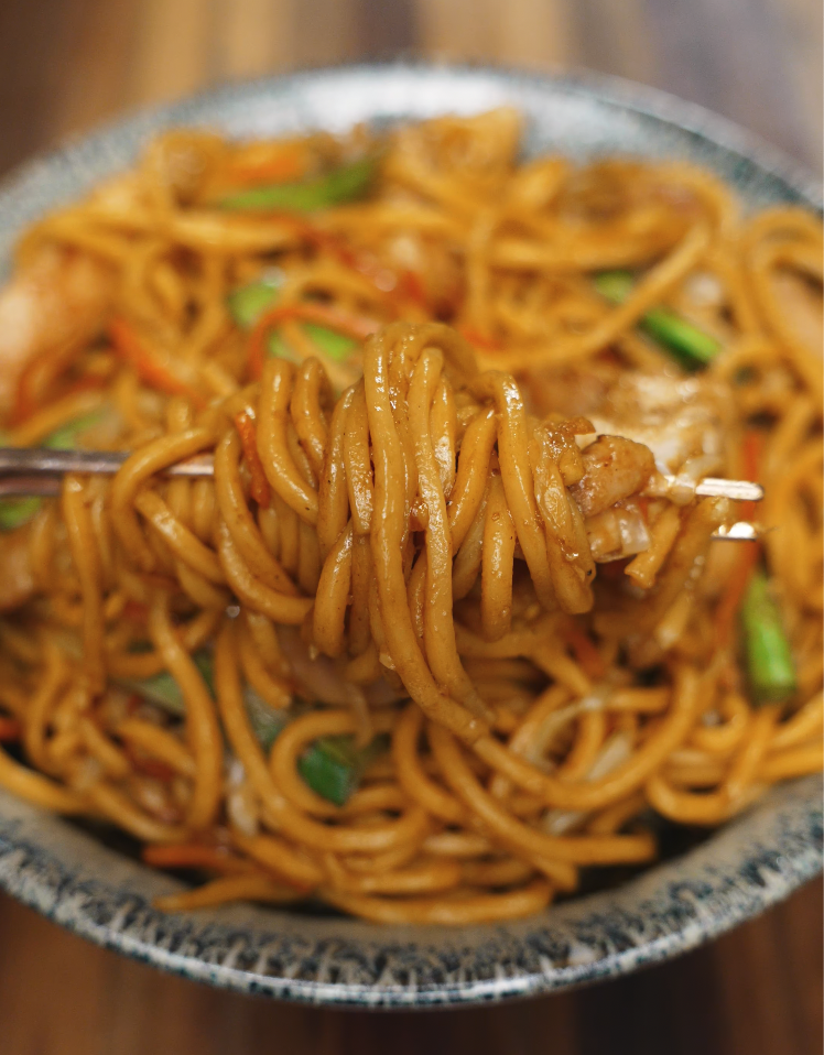 Close-up shot of a fork twirling up saucy lo mein noodles with chicken and vegetables, capturing the irresistible texture and flavor of this homemade takeout favorite.