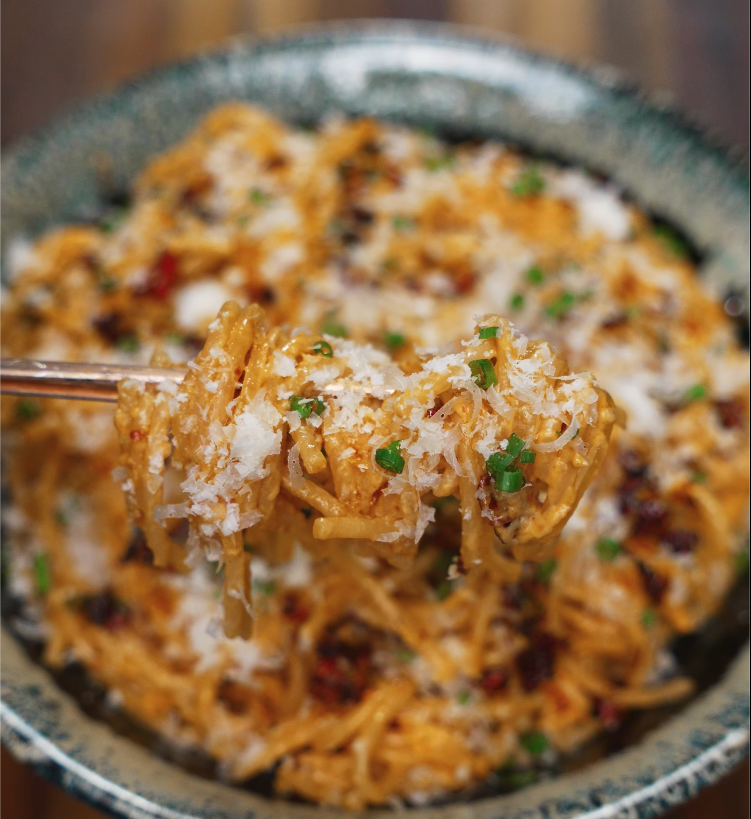 Close-up of a forkful of chili oil caramelized onion pasta topped with parmesan and scallions.