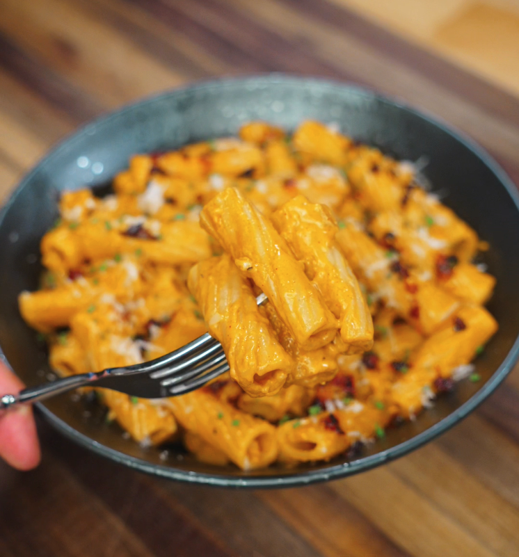 A fork lifting a bite of creamy gochujang rigatoni from a full bowl, showcasing the rich orange sauce clinging to each tube of pasta.