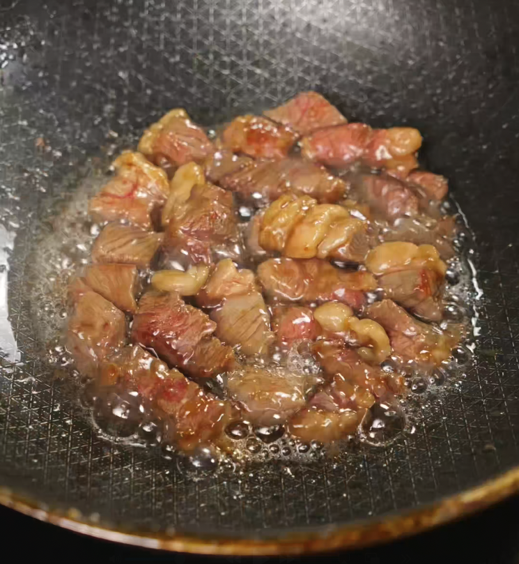 Marinated beef cubes sizzling in hot oil in a nonstick pan as they develop a golden-brown sear for garlic steak fried rice.