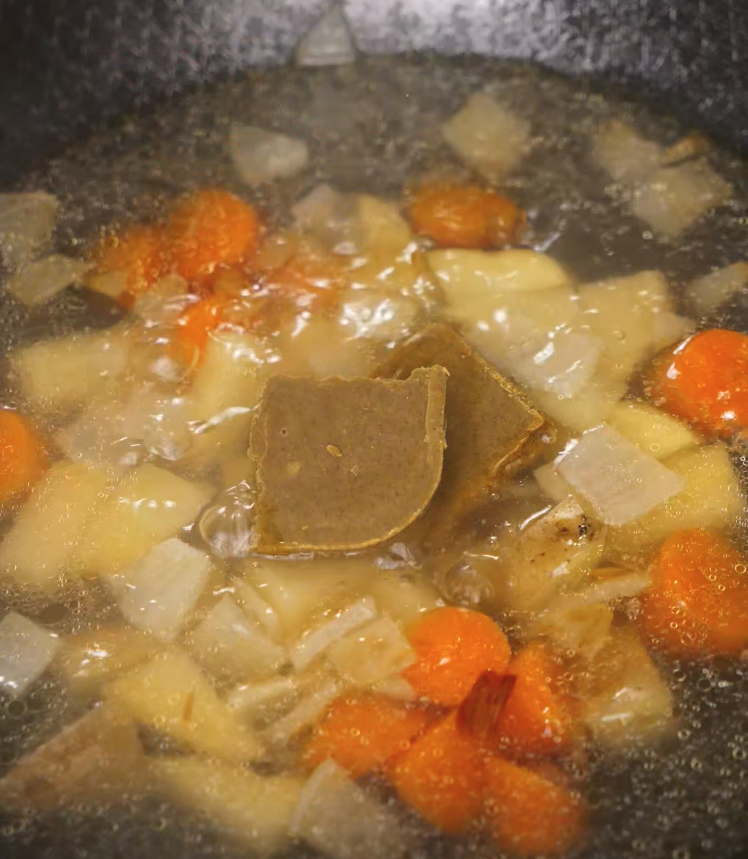 Japanese curry roux cubes melting into a pot of simmering potatoes, carrots, and onions.