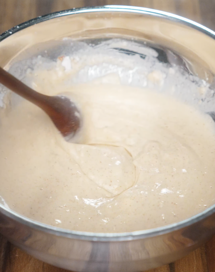 Stirring together a smooth, creamy batter in a silver mixing bowl for coating the chicken before frying.