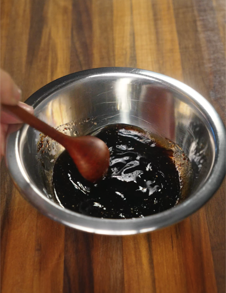 Stirring together dark soy sauce, oyster sauce, and other seasonings in a metal mixing bowl to create the rich and savory sauce base for Beef Chow Fun. This sauce coats the noodles and beef to deliver bold umami flavor in every bite.
