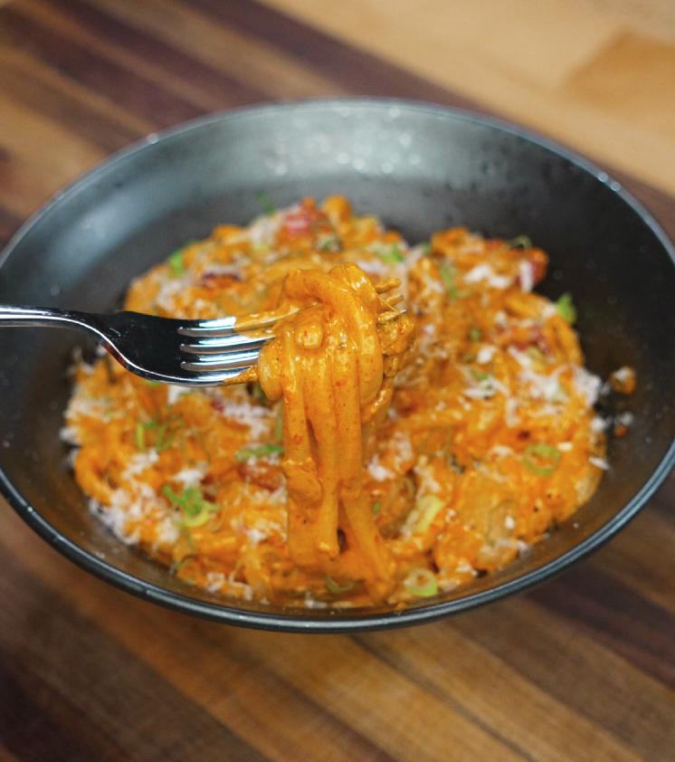 A fork lifting a bite of creamy kimchi noodles, showcasing the thick sauce clinging to the chewy udon noodles.