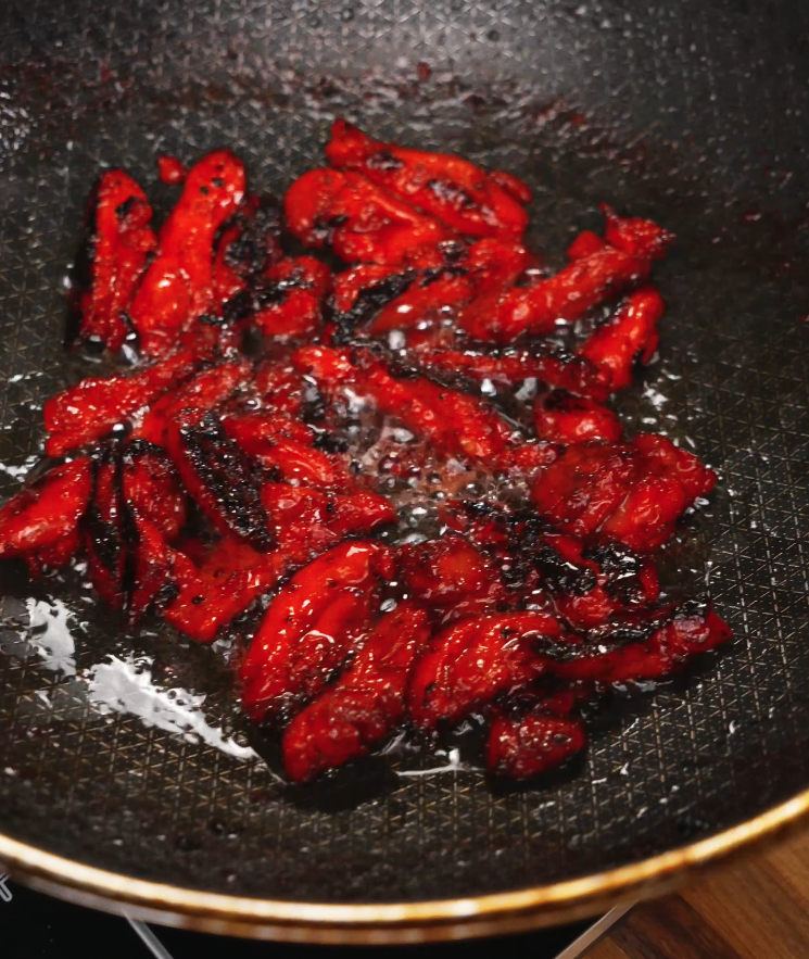 Strips of marinated Chicken Tocino sizzling in a pan, developing charred edges and a sticky glaze. This caramelization is essential for bringing out the sweet and smoky flavors of the dish.