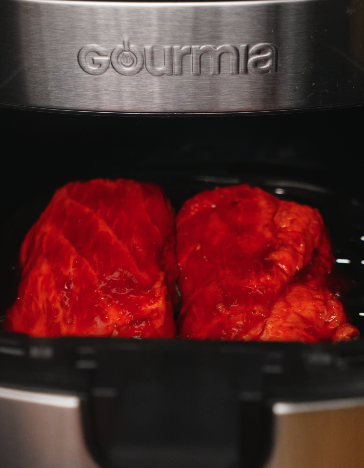 Two marinated pork shoulder pieces placed in a Gourmia air fryer, ready to cook until caramelized and tender.