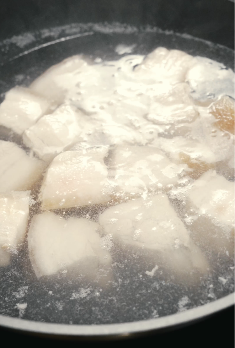 Raw chunks of pork belly simmering in a pot of water, a step used to remove impurities before braising.