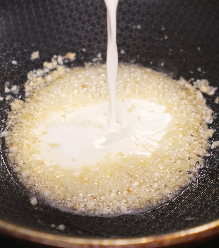 Pouring starchy pasta water into the sautéed garlic mixture in a hot skillet to begin creating the sauce.