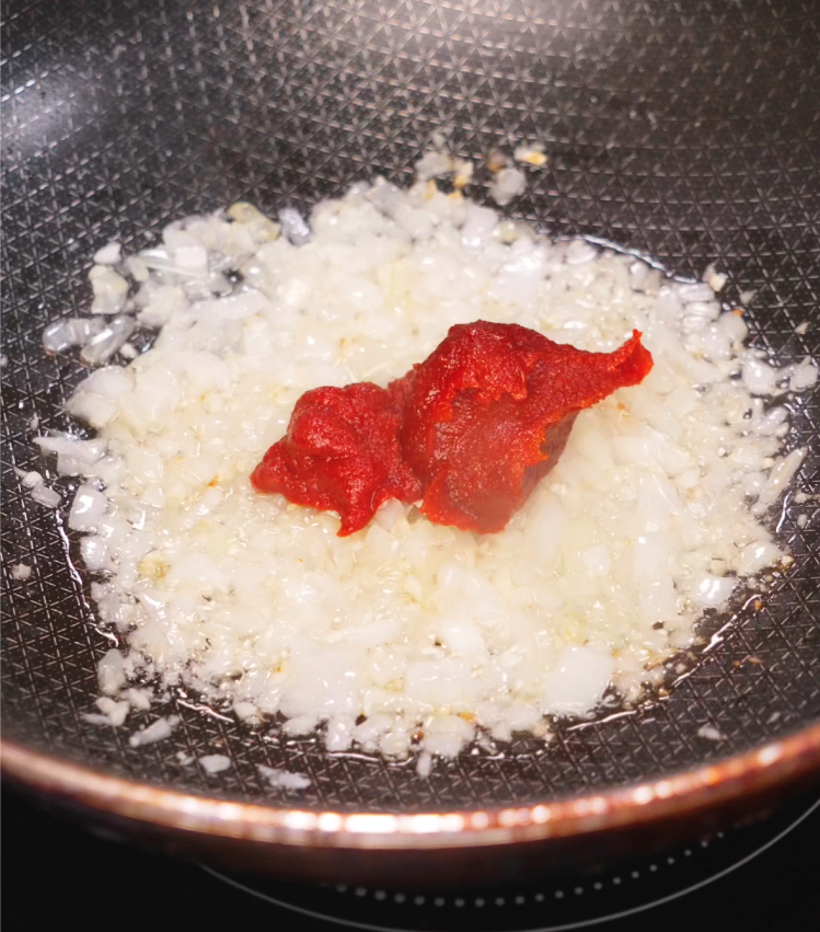 A close-up of sautéed diced onions with vibrant red gochujang and tomato paste sizzling in a nonstick skillet, creating a savory, spicy base for the sauce.