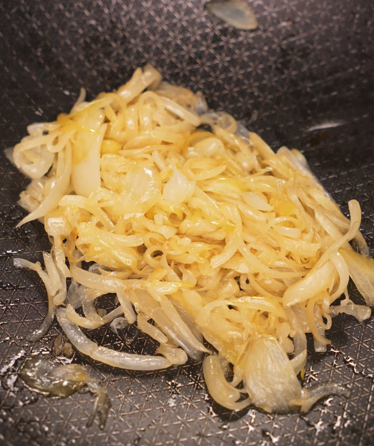 Thinly sliced onions caramelizing in oil in a nonstick pan for the base of the chili oil pasta.