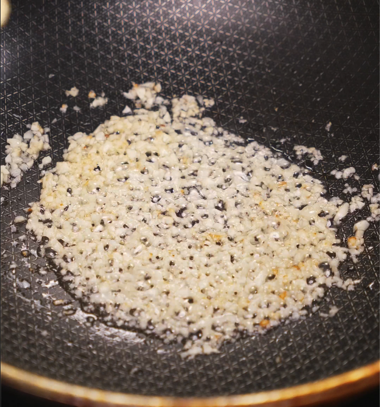 Garlic sizzling and turning golden brown in oil inside a non-stick black skillet with a patterned surface.