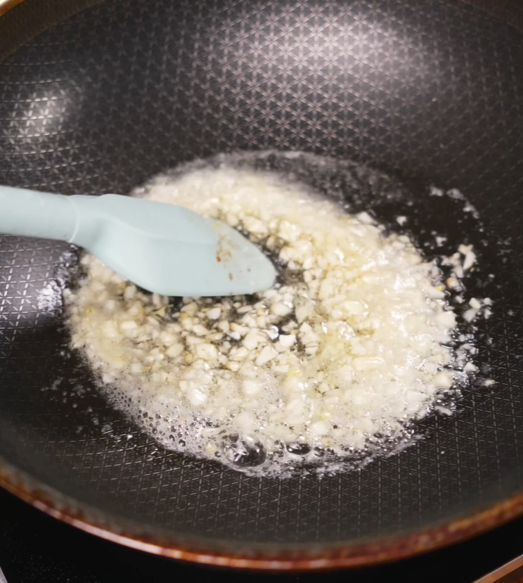 Minced garlic gently sizzling in a pool of melted butter in a nonstick skillet, the base for garlic butter noodles being prepared.