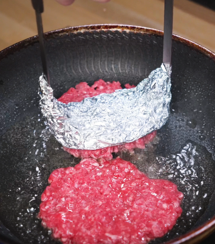 Beef balls smashed flat with foil-wrapped spatula in a hot skillet to create crispy smash burger patties, key for the signature sear.