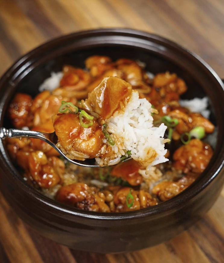 A spoonful of glossy, thick ginger braised chicken is being drizzled over a fresh bowl of steamed white rice, showcasing the final serving step.