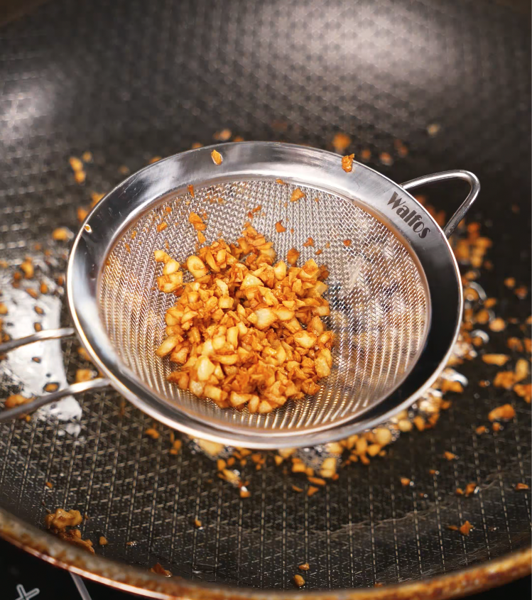 A strainer filled with freshly fried golden brown minced garlic being held above a pan, ready to be used as a crispy topping for garlic steak fried rice.