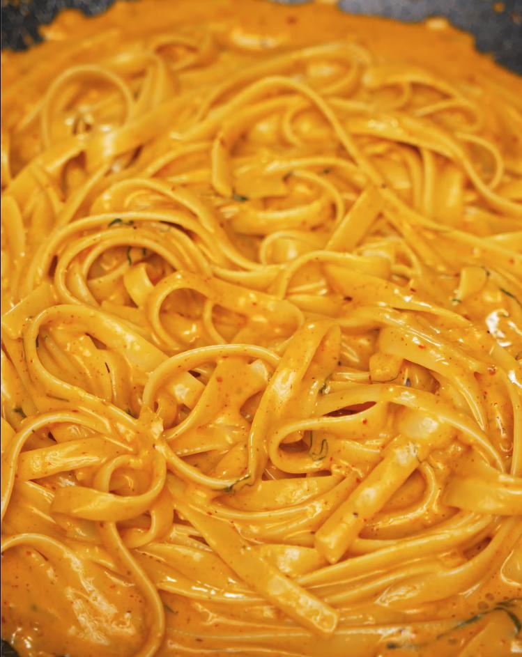 The fettuccine noodles being tossed in the creamy, spicy gochujang Alfredo sauce until fully coated and glossy.