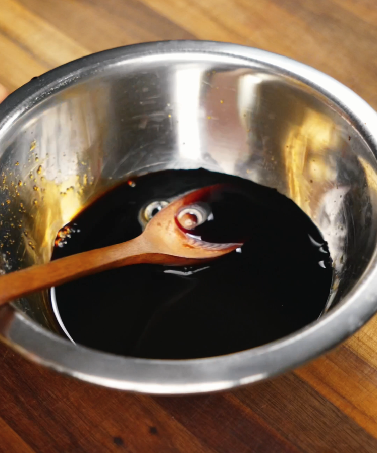 A dark savory sauce blend in a metal mixing bowl with a wooden spoon, made from soy sauce, oyster sauce, and mirin, ready to flavor the beef yaki udon.