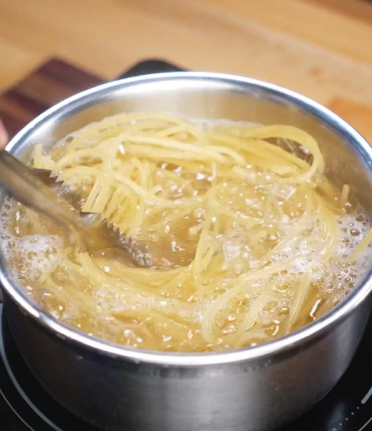 Spaghetti noodles boiling vigorously in a stainless steel pot on the stovetop, stirred with tongs to prevent sticking. These noodles serve as the base for the creamy peanut butter chicken noodles and are cooked just shy of al dente for a perfect bite.